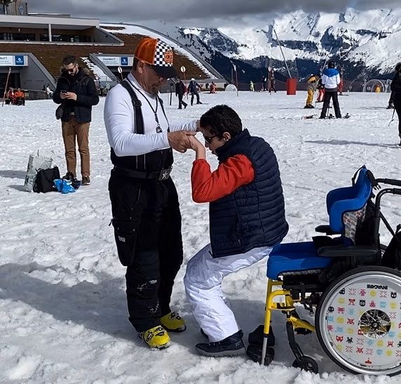 visuel Marc Gostoli medecin dans la neige avec un enfant en fauteuil roulant